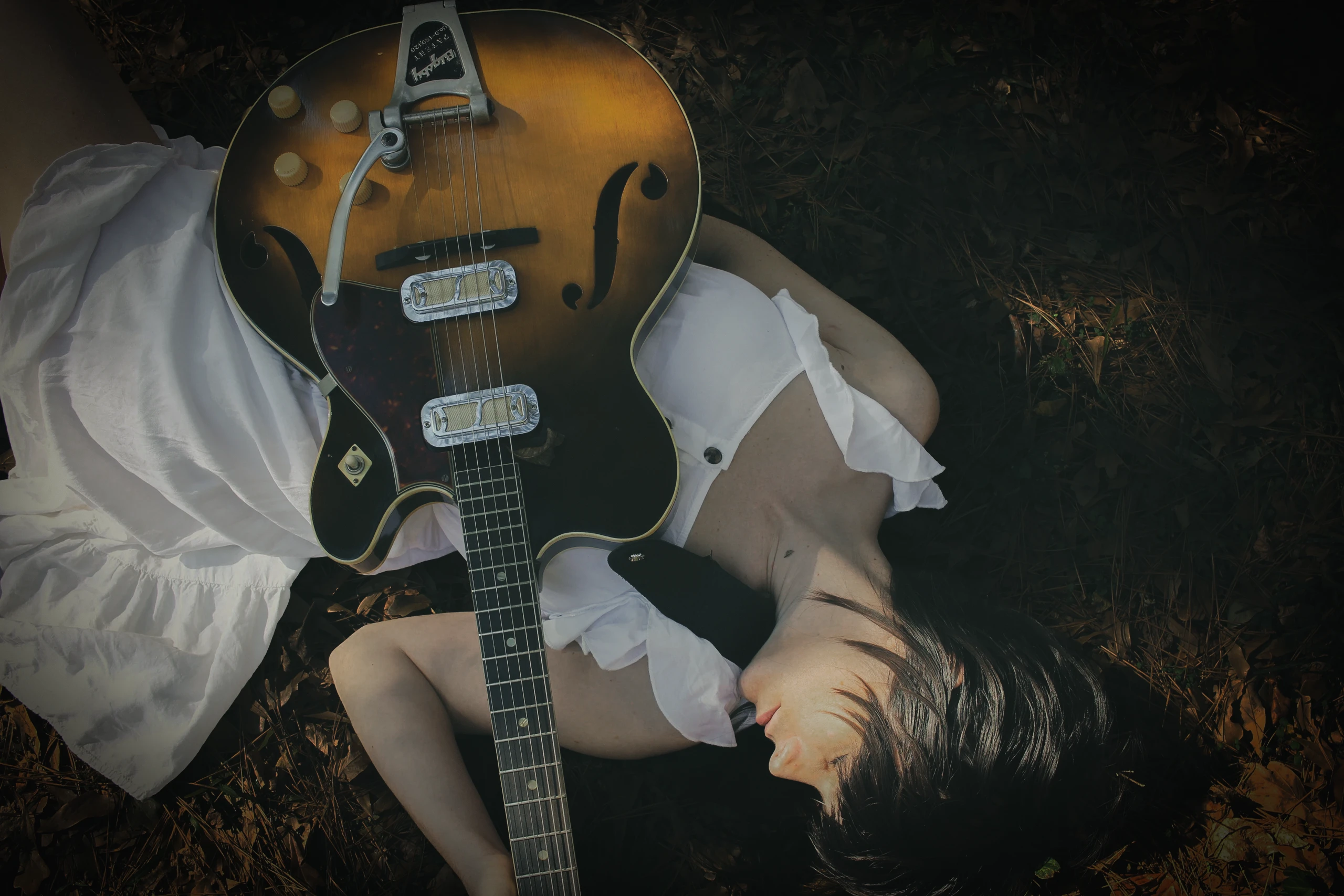 Image of a musician holding a guitar while lying in the grass